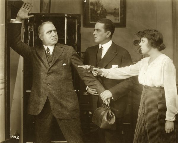 The actress Nell Craig holds a revolver on Ernest Maupain while Richard Travers looks on in a scene still from the 1916 Essanay film "In a Looking Glass."