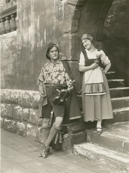Original caption on reverse of print reads:
"Principals in Corsican drama, 'A Daughter of Caliente.' Douglas Gerrard, producer and actor and his leading lady, Ruth Clifford, on one of the sets at Universal City."

Gerrard and Clifford are in traditional peasant costumes. He holds a violin and she a flower.