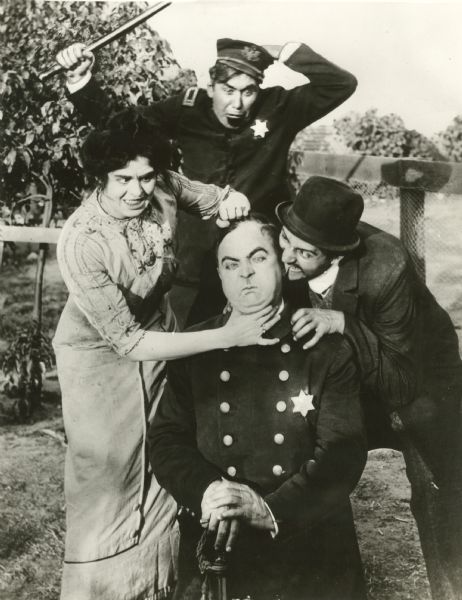 Murphy the cop (played by Fred Mace) kneels as he is tormented by his wife (Dot Farley) who chokes him with one hand and raps him on the head with the other and Cohen the pawn broker who bites his ear (Henry Lehrman). Coming up from behind is a police captain with a raised nightstick (Mack Sennett). Lehrman directed and Sennett produced "Murphy's I.O.U." a 1913 Keystone Comedy.