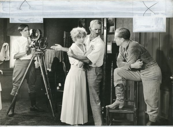 This appears to be a "Kitty Kelly, M.D." production still from 1919. If so, the cameraman behind the Bell & Howell model 2709 is probably Eugene Gaudio. The original caption reads:
"Howard Hickman, husband and director of Bessie Barriscale, shows leading man Jack Holt how to make love to Mrs. Hickman."
