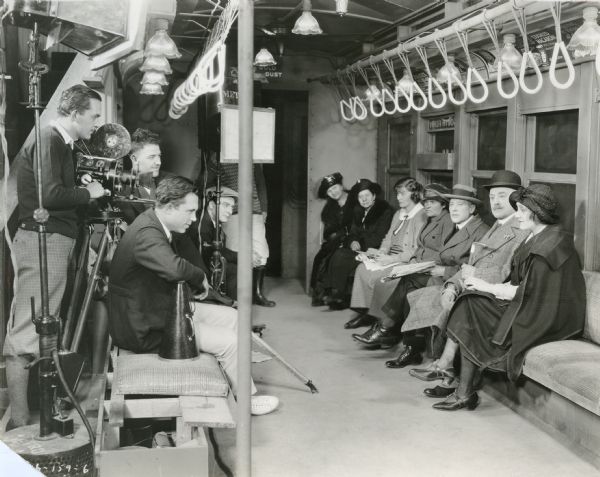 On the left, cameraman Chester A. Lyons cranking a Bell & Howell model 2709 and director King Vidor seated next to his megaphone. On the right, a line of actors on a bench in a subway car set with the star Laurette Taylor seated at the end.