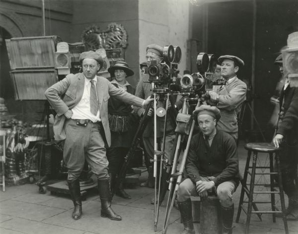 Left to right: Cecil B. DeMille (director), Anne Bauchens (film editor), Karl Struss (cinematographer, in glasses), Alvin Wyckoff (cinematographer), and other crew members working in the Siamese temple set of "Fool's Paradise." Both Struss and Wyckoff are using Bell & Howell model 2709 cameras.