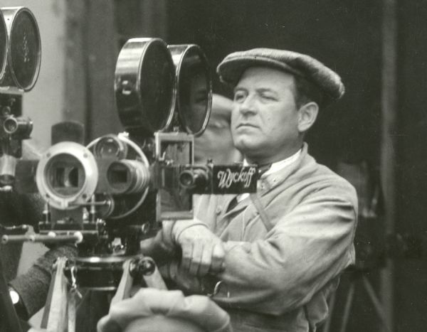Cinematographer Alvin Wyckoff stands next to his Bell & Howell model 2709 motion picture camera on a set for the Cecil B. DeMille silent feature "Fool's Paradise" (Famous Players-Lasky 1921).