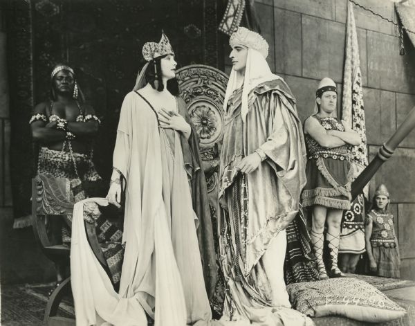Betty Blythe as the Queen of Sheba and Fritz Leiber as King Solomon stand before their thrones and face one another with attendants in the background.