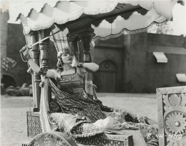 The Queen of Sheba, played by Betty Blythe, sits in a cart and holds a sword above her head in William Fox's "Queen of Sheba" (1921).