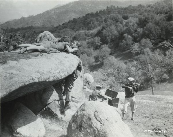 Pauline Starke (as Emmy) and Arthur Rankin (as Bud) pose in a production still from the 1925 Metro-Goldwyn-Mayer production "Sun-Up." Behind them are two on-location musicians, a violinist and a portable organ player.