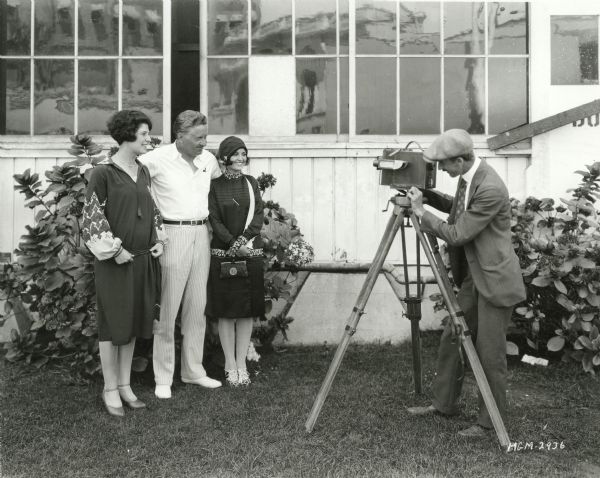 Director Fred Niblo poses between two unidentifed young women in front of a cameraman and his Debrie Interview motion picture camera in a Metro-Goldwyn-Mayer publicity still.