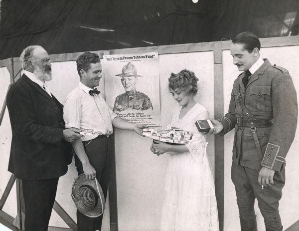 Original caption: "Mary Pickford getting tobacco and cigarettes for the soldiers. In addition to supplying her own adopted contingents, Miss Pickford has sent thousands of smokes to the boys in the trenches. The others in the picture are Norman Kerry, in uniform; Marshall Neilan, her director and Theodore Roberts."