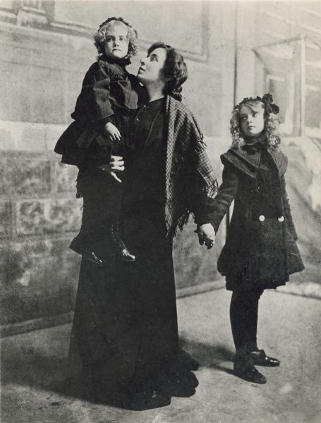 Mary Robinson McConnell carries her daughter Dorothy Gish and holds her older daughter Lillian Gish by the hand in front of theatrical scenery.