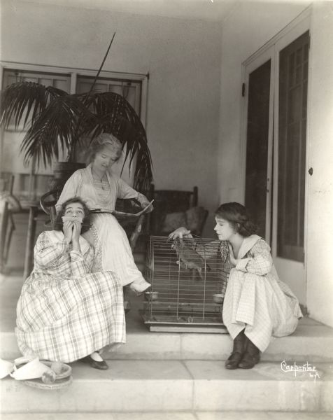 Original caption: "Mrs. Gish & her two talented girls. Dorothy is entertaining the parrot with a comb solo while Lillian does something to Poll."