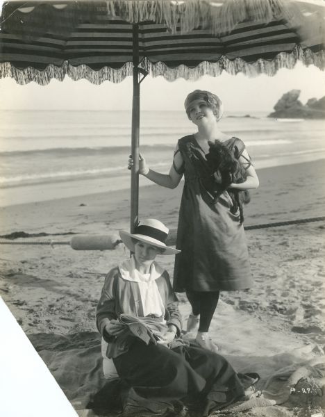 Silent film actress Mary Miles Minter, her dog, and her mother Charlotte Shelby at the beach under an umbrella.