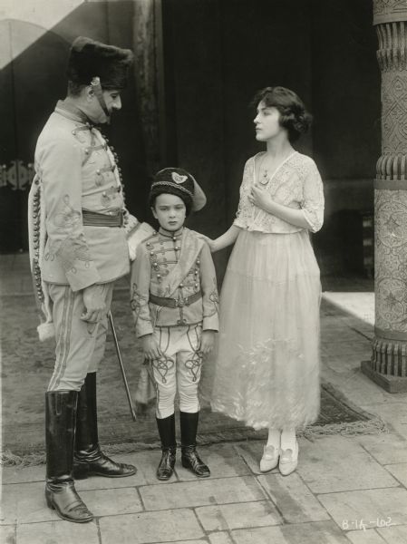 Original caption: "Evelyn Nesbit and her son Russell Thaw. Miss Nesbit is now a film star, and in her first production, 'The Woman Who Gave' which she made for William Fox, she has as one of her supporting company, her son, Russell Thaw. Some of the scenes of the picture are laid in Bulgaria, which accounts for the costume which Russell is wearing in the accompanying photograph."