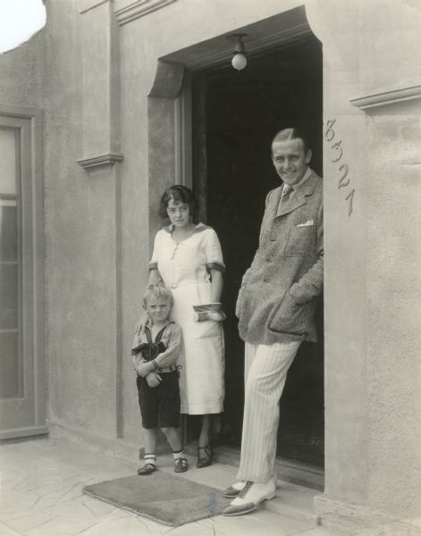 Original caption: "Wallace Reid, Paramount star, his wife, formerly Dorothy Davenport, and their son William Wallace Reid Jr., otherwise known as Bill, at the door of their Hollywood home."