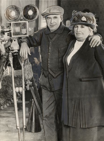 Silent film producer and director Mack Sennett, wearing at least two sweaters, with his mother and a Bell & Howell motion picture camera in a heavily retouched press photograph.
