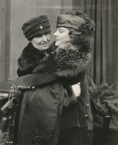 The silent film star Gloria Swanson and her mother Adelaide Klanowski Swanson embrace in a Famous Players-Lasky publicity still. Both wear winter coats with fur collars and hats.