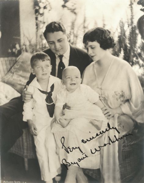 Silent film actor Bryant Washburn and his wife the actress Mabel Forrest sit on a wicker sofa with their sons Bryant Washburn, Jr. (in a sailor suit) and Dwight Ludlon Moodey Washburn, an infant. The print bears the inscription "Very sincerely Bryant Washburn" (made by a rubber stamp or machine).