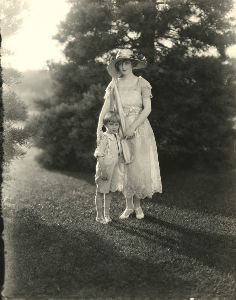 Silent film star Claire Windsor in a lacy summer dress and sun hat with her small son Billy outdoors.