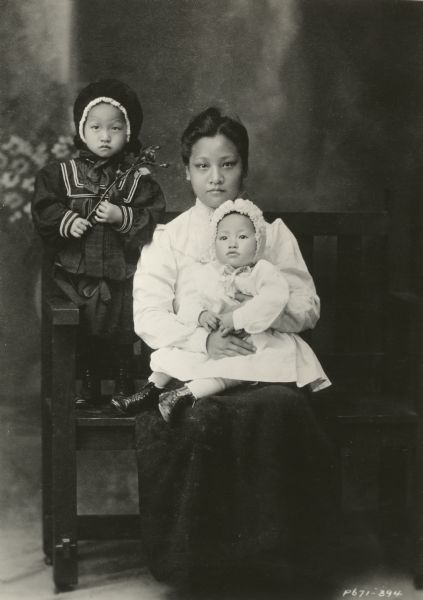 1934 caption from Paramount Productions: "ANNA MAY WONG IN ARMS. The large-eyed little girl, seated in her mother's lap, is Anna May Wong, Chinese film star, who has grown up to be rated the most sophisticated woman in the world, and the outstanding Oriental beauty. Anna May has just completed a Hollywood trip from London to complete 'Limehouse Blues' with George Raft and Jean Parker. Standing in this photo is Anna May's sister, Ying Wong. The mother, who died three years ago, was Mrs. Wong Sam Sing."