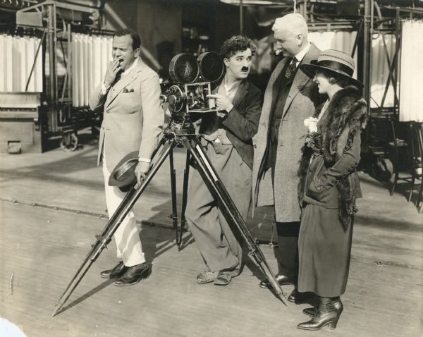 From left to right: Douglas Fairbanks, Charlie Chaplin, Oscar Amos Price, president of the United Artists Corporation, and Mary Pickford. Mr. Chaplin explains the mechanism of the Bell & Howell Model 2709 motion picture camera to Mr. Price, but Mr. Fairbanks is dying of boredom.