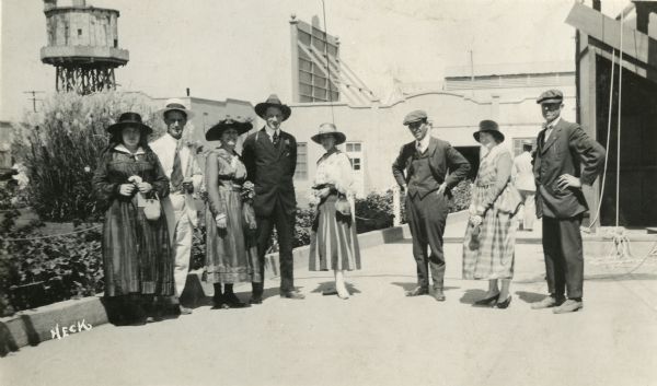 Seven well-dressed tourists visit Universal City and pose with actor Rube Miller, one of the original Keystone Cops. A water tower is visible behind them.