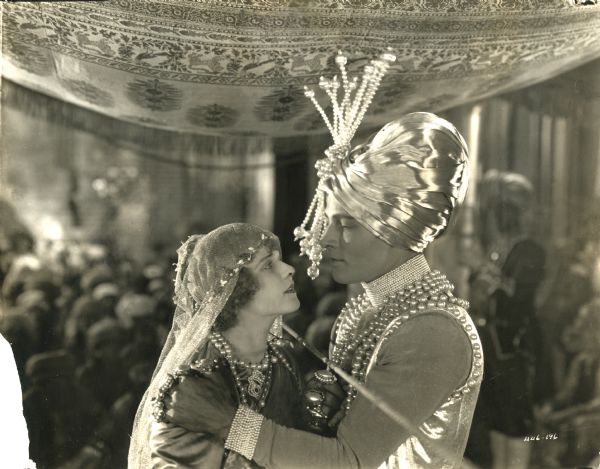 The Maharajah of Dharmagar (played by Rudolph Valentino) embraces Molly Cabot (Wanda Hawley) in a scene still from "The Young Rajah" (1922). Valentino wears a white satin turban and innumerable pearls.