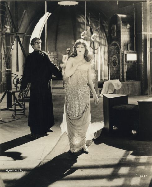 A scene still set in Doctor Demetrius's laboratory from the silent film "The Young Diana." Diana May (played by Marion Davies) has just been rejuvenated by Dr. Dimitrius (Pedro de Cordoba). Davies wears a strapless dress covered with sequins.