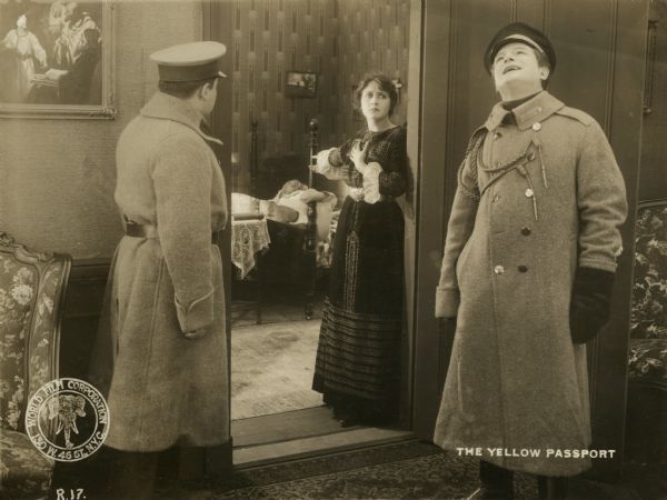 Sonia Sokoloff (played by Clara Kimball Young) stands in a doorway and gestures toward a bedroom to two police officers. The officer with his head thrown back in laughter is Fedia (John St. Polis).