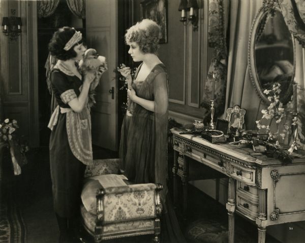 Margaret Vane (played by Norma Talmadge) stands by her dressing table and fusses with the little Pomeranian dog held by her maid in a scene still from "Yes or No."