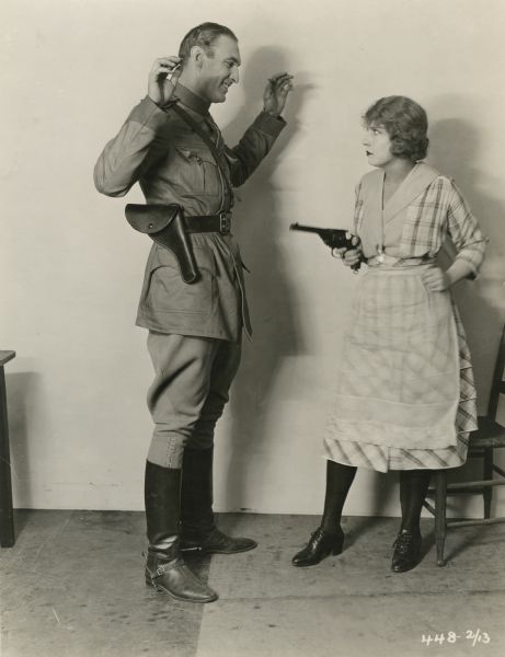 Iris Champneys (played by Dorothy Dalton) holds a revolver on Jock MacKeinney (Maurice "Lefty" Flynn) in a publicity still from "The Woman Who Walked Alone." Flynn wears a cavalry uniform with boots and spurs, jodhpurs, and a Sam Browne belt.