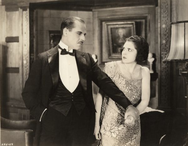 Lord Raa (played by Jack Holt) aggressively grasps the wrist of Mary MacNeill (Katherine MacDonald) in a scene still from "The Woman Thou Gavest Me." They glare at one another.
