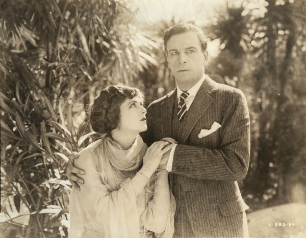 Mary MacNeill (played by Katherine MacDonald) holds the hand of Martin Conrad (Milton Sills) and looks lovingly at his face. They are outdoors in a garden in this scene still from the Famous Players-Lasky production "The Woman Thou Gavest Me."
