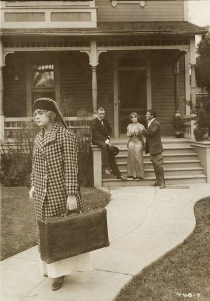 Kathlyn Williams, in a checked winter coat and carrying a suitcase, walks away from two men and a woman on the front steps of a Victorian house in a scene still from "A Woman Laughs" (Selig 1914). The actors on the steps appear to be, from left to right, Charles Clary, Bessie Eyton, and Harry Lonsdale.