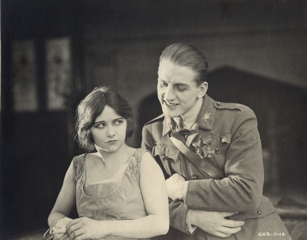 In a publicity still from "The Wonderman," Henri D'Alour (played by Georges Carpentier, the French boxer, aviator, and actor) stands grinning over the shoulder of Dorothy Stoner (Faire Binney). Carpentier wears an aviator's uniform decorated with the French Médaille Militaire and Croix de Guerre.