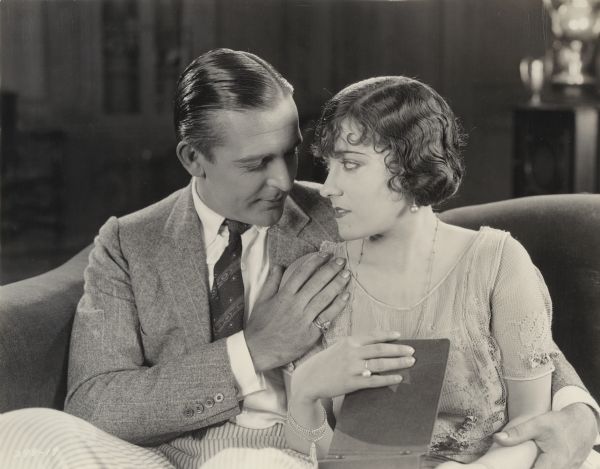 Anatol Spencer and Vivian his wife (played by Wallace Reid and Gloria Swanson) sit on a sofa and look through a photograph album in a scene still from the 1921 Cecil B. DeMille production "The Affairs of Anatol."