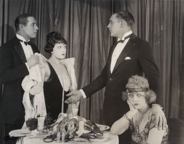 In this scene still from Cecil B. DeMille's 1921 production "The Affairs of Anatol," the actors Elliot Dexter, Gloria Swanson, Wallace Reid, and Wanda Hawley are dressed in evening wear in the Green Fan Cafe.