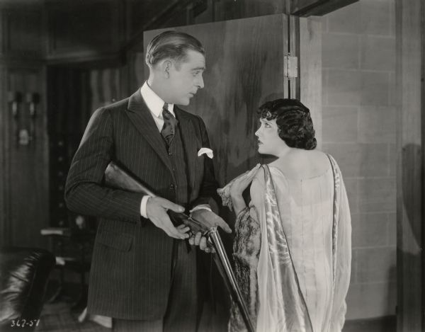 Anatol Spencer (played by Wallace Reid) stands in a doorway with his wife Vivian (Gloria Swanson) in this scene still from Cecil B. DeMille's 1921 production "The Affairs of Anatol." Reid has a double-barreled shotgun in his hands.