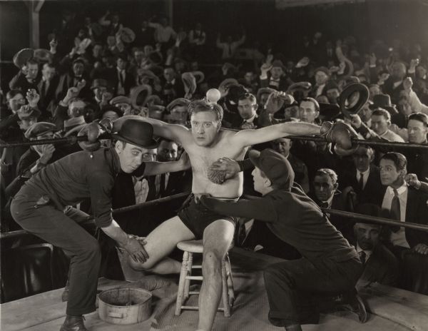 The boxer Tom Harper (played by Frank Mayo) is in his corner between rounds with his corner men. Behind them is lively crowd of male spectators in a scene still from "Afraid to Fight."