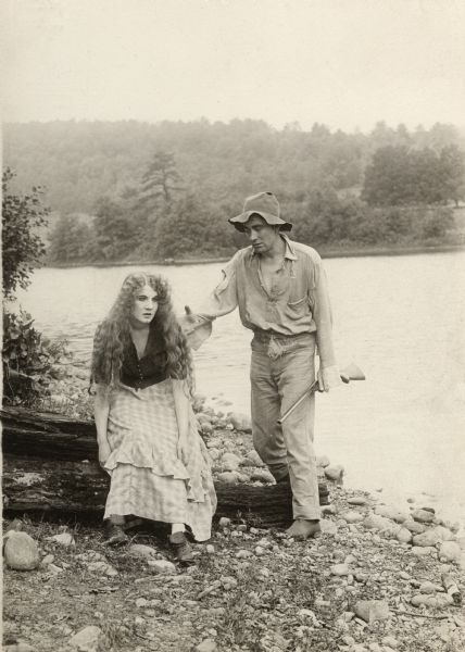 Florence Lawrence and Owen Moore (as Margie and Rob) are dressed in rough county clothes for the rural Southern drama "After All." They are on the shore of a lake. Moore caries a single-barrel shotgun.