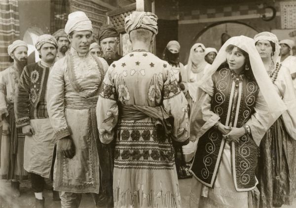 Jack Stanton (played by Antonio Moreno) is being married to Faimeh (Edith Storey) in a Turkish ceremony in a scene still from "Aladdin from Broadway." Moreno and Storey are costumed in Turkish style as are the crowd witnessing the ceremony in turbans and headscarves.