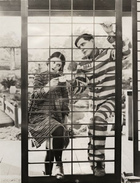 The silent film actors Viola Dana and Bert Lytell, wearing costumes for different productions, knock their coffee cups together in a toast that is apparently a reference to Prohibition. Lytell wears a striped prisoner uniform for the title role in "Alias Jimmy Valentine" and Dana is dressed as an adolescent for her role as Eliza in "Dangerous to Men."