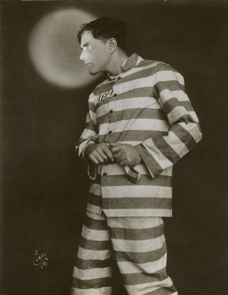 Bert Lytell, his face illuminated by a small spotlight, poses in a prisoner's striped uniform in a publicity still for the silent film "Alias Jimmy Valentine" (Metro 1920).