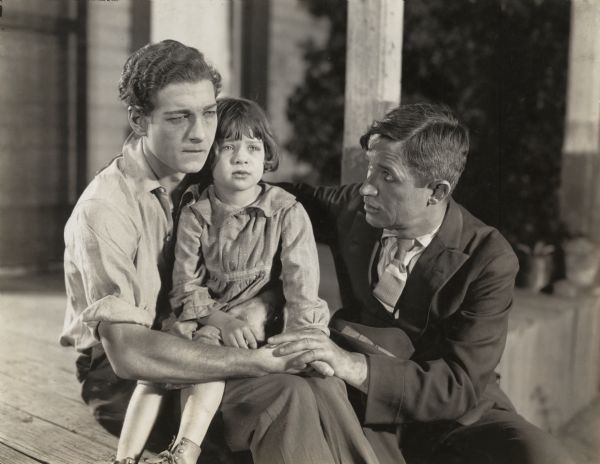 Will Rogers, playing the school teacher Sam Lyman at right, comforts Cullen Landis and a young Mary Jane Irving in a scene still for "Almost a Husband."