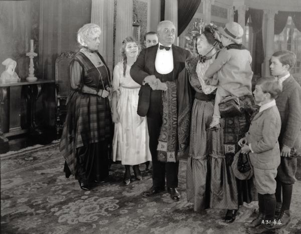 Amarilly Jenkins's family arrives for tea at the mansion of Mrs. Stuyvesant Phillips. From left to right: Mrs. Stuyvesant Phillips (played by Ida Waterman), Amarilly Jenkins (Mary Pickford), unidentified actor in background, Mrs. Stuyvesant's butler (unidentified actor), Mrs. Americus Jenkins (Kate Price), Jenkins' toddler son carried by Kate Price (unidentified), Jenkin's son (Wesley Barry), and older son (Frank Butterworth).