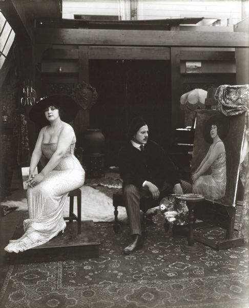 In this publicity still for "Ambrose's Cup of Woe," Edgar Kennedy plays an artist in black velvet jacket and beret who sits contemplating his painting with his palette in hand. May Emory is his model. She wears a low cut dress and large hat.