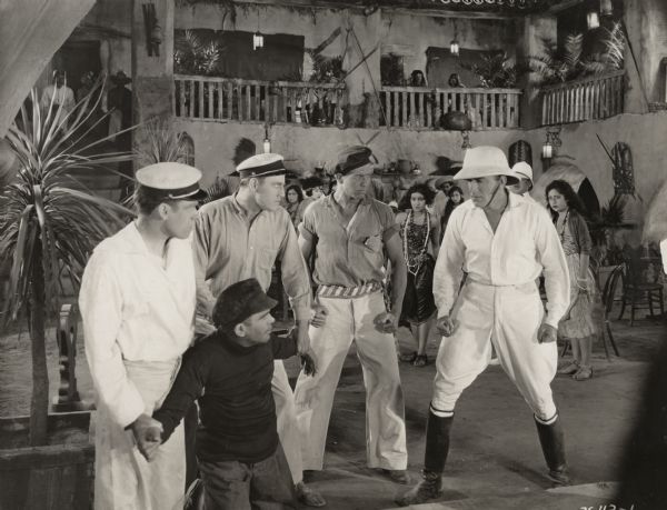 Frank Mayo, wearing a white pith helmet, white shirt, and white jodhpurs, confronts a group of four sailor ruffians in a town on a South Sea island in a scene still from "The Altar Stairs."