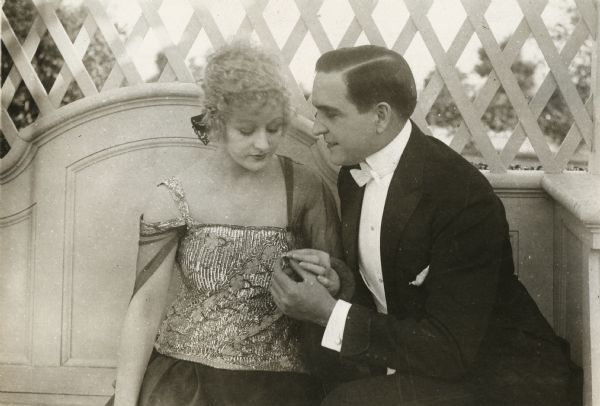 Ida Payne (played by Grace Darmond) is given a ring by Willard Geddie (Earle Williams) as they sit in a garden seat in a scene still for "An American Live Wire."