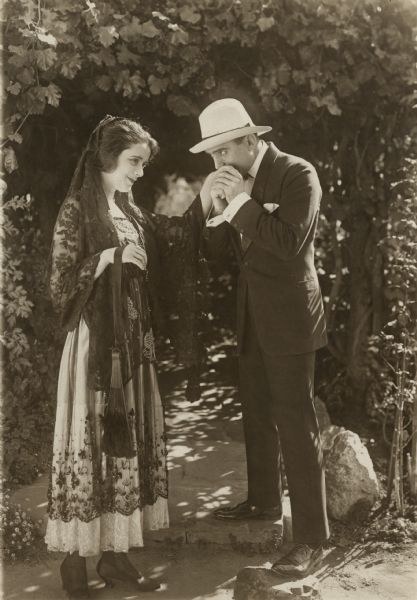 Juana de Castalar (played by Alma Reubens) has her hand kissed by Blaze Derringer (Douglas Fairbanks) in a scene still for "The Americano." Reubens is costumed in a Spanish style lace dress and black mantilla.