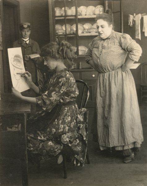 Florence Lawrence makes a crude drawing as her mother and a telegram delivery man watch in a scene still from "The Angel of the Studio."
