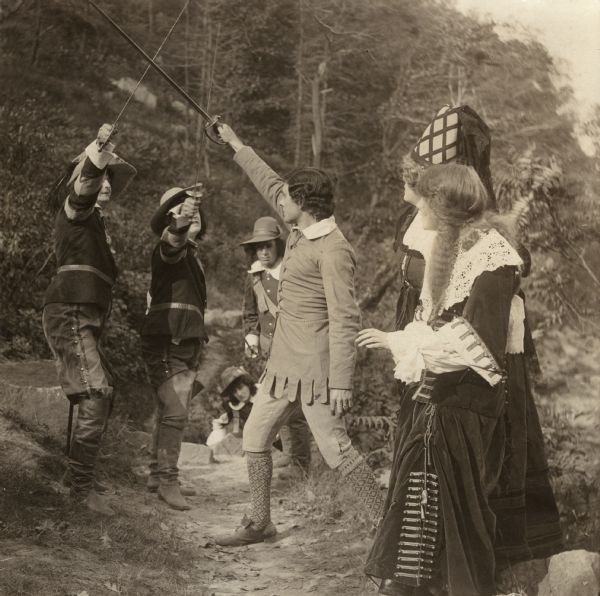 In this scene still four men in Renaissance costume fight with swords while two women watch. The actress in the foreground is Florence Lawrence.