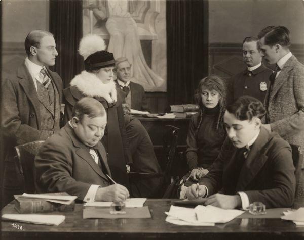 In this scene still for "Angels Unawares," Ruth Stonehouse plays Freckles, a street waif, who sits forlornly in a courtroom complete with a judge, lawyers, clerks, and a police officer. The other actress in the scene may be Madge Kearns.